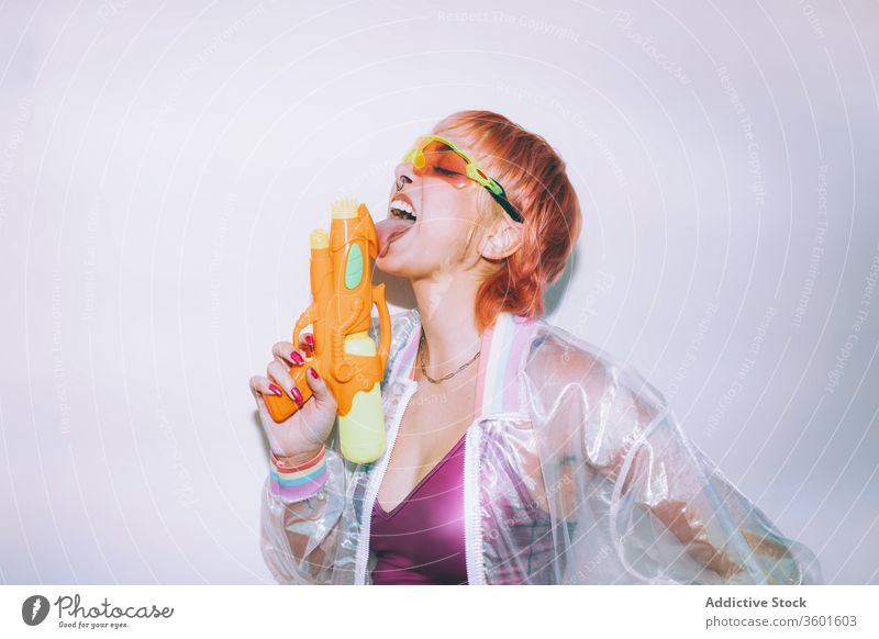 Retro futuristic woman licking water gun style eyes closed young weapon outfit retro female model dyed hair trendy jacket sunglasses pistol angry vintage