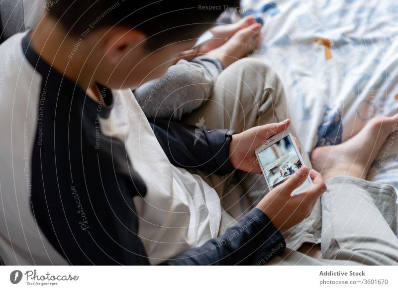Crop siblings using smartphone on bed watch cartoon relax home children brother cozy childhood device gadget rest browsing internet chill surfing connection