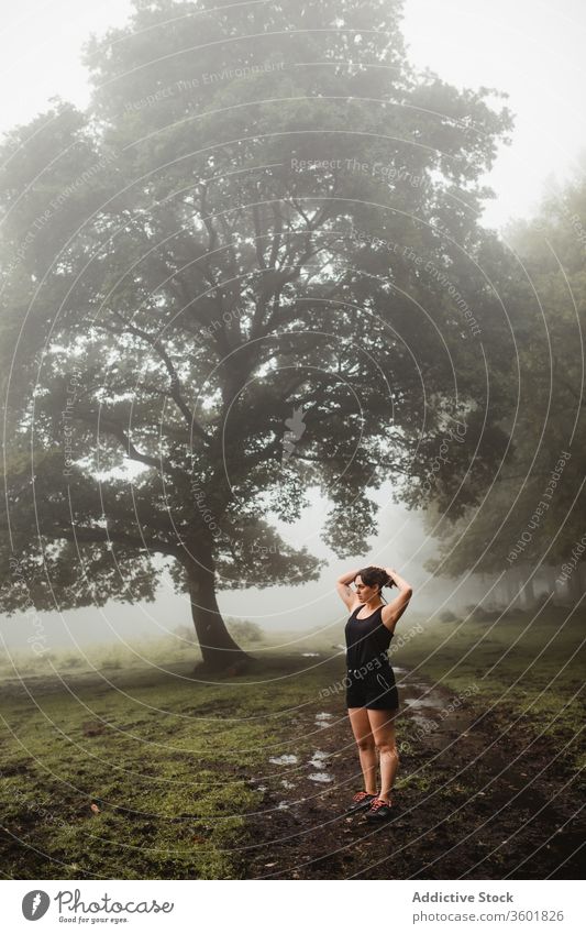 Fit sportswoman warming up during workout in forest training warm up exercise woods morning fog activewear dirty path healthy endurance athlete wellbeing