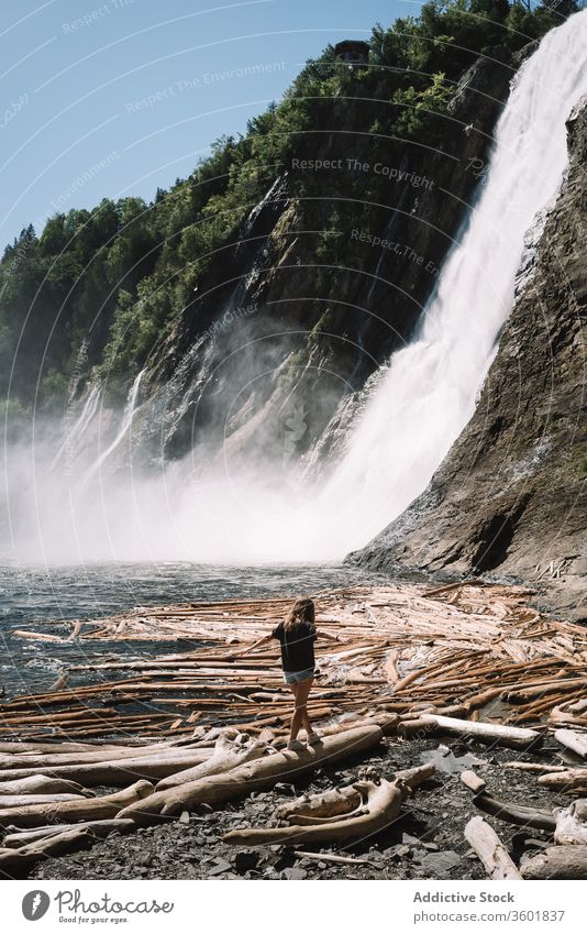 Unrecognizable lonely female teenager walking along river shore against waterfall girl beach fresh snag travel cascade nature tranquil wilderness flow rocky