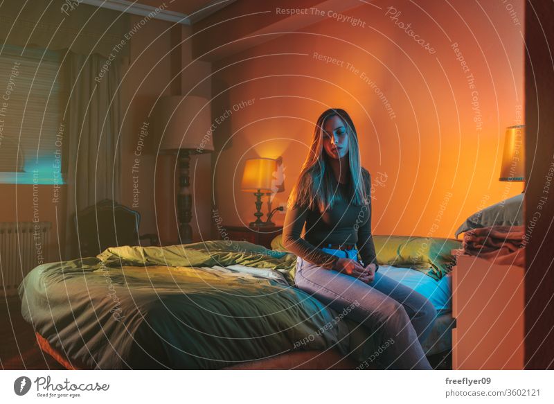 Young woman sadly sitting alone on the bed late at night portrait female quarantine depression pillow coronavirus covid-19 isolation self-isolated insomnia blue