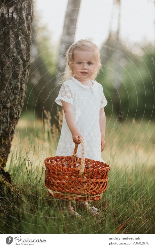 Beautiful baby girl walking in a sunny garden with a basket. little girl in a white dress with a basket in the park spring portrait kid beauty child field