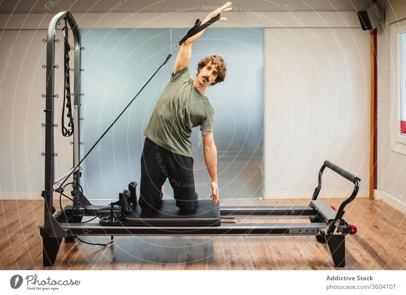 Sportive man using pilates reformer during training stretch sporty activewear resist band machine sportsman athlete exercise workout fitness healthy sportswear