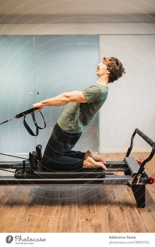 Sportive man using pilates reformer during training stretch sporty activewear resist band machine male sportsman athlete exercise workout fitness healthy