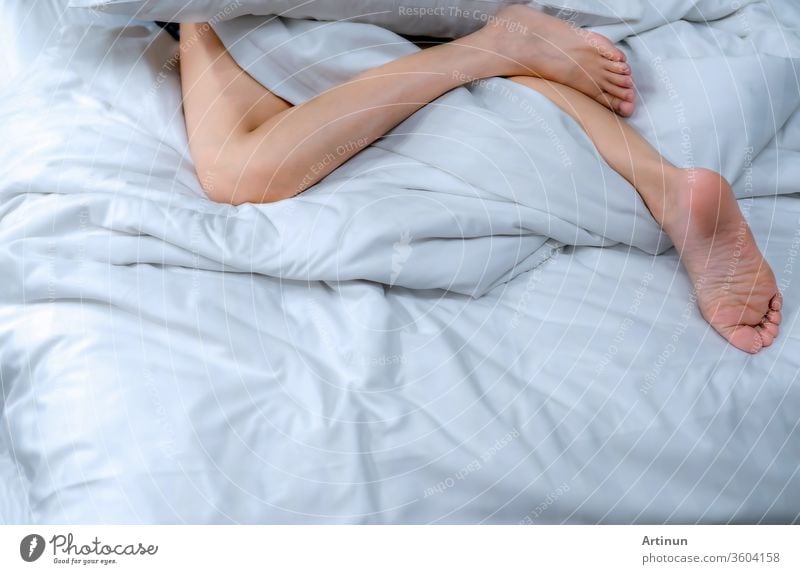 Close up woman bare feet on the bed  over white blanket and bed sheet in the bedroom of home or hotel. Sleeping and relax concept. Lazy morning. Barefoot of woman lying on white comfort bed and duvet.