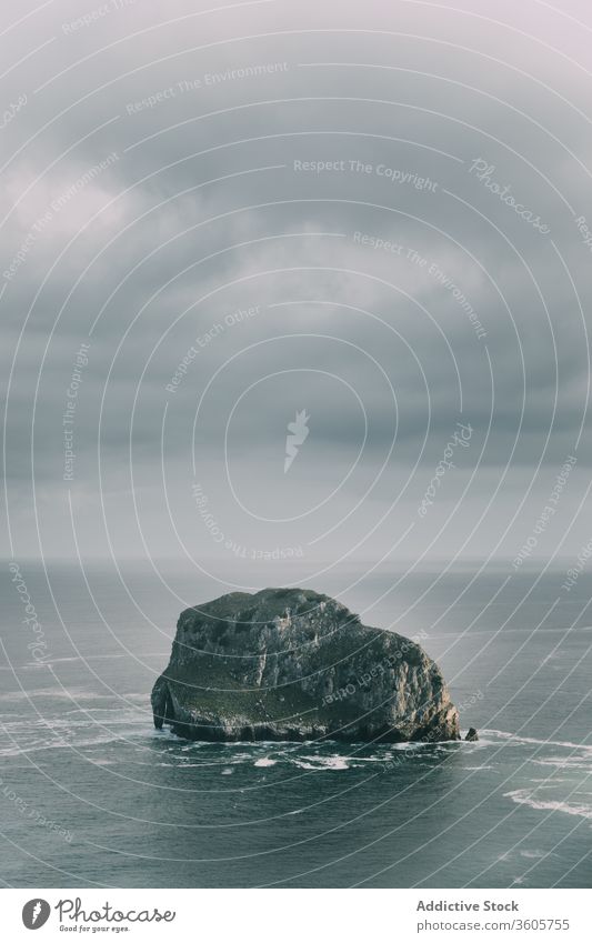 Rocky formation in center of sea under cloudy sky rock seascape breathtaking overcast picturesque nature scenery magnificent beauty wave harmony rocky paradise