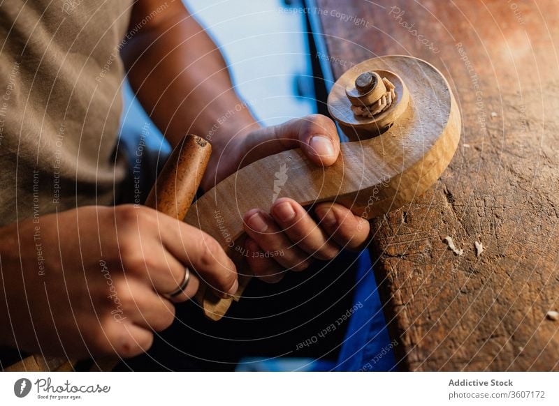 Crop workman crafting violin head using chisel in modern work studio carving craftsman tool workshop hand process handmade swirl bit wooden shape creative