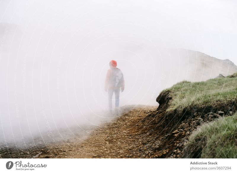 Unrecognizable male traveler in foggy highlands man walk mountain mist explorer mystic landscape iceland weather road cold season outerwear warm clothes tourism