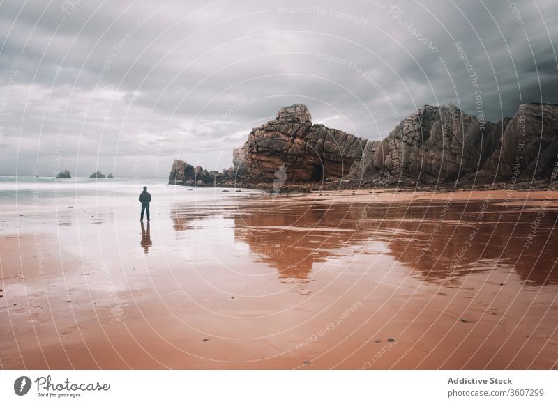 Lonely man standing on sandy seashore with rocky cliffs rough traveler lonely overcast gloomy nature coast reflection male sky cloudy stormy severe tourism