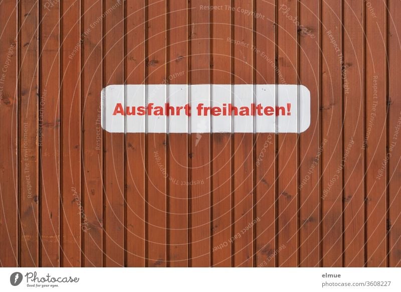 white sticker with red print "Keep exit free!" on a brown wooden wall Keep the exit clear! stickers Clearway writing letter Wooden wall Private