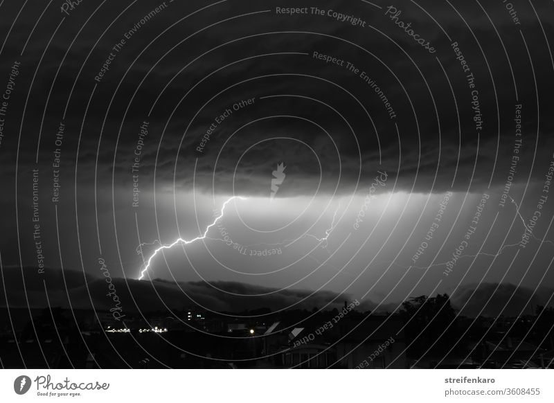 Enormous lightning can be seen in the black and white sky between the mighty cloud layers Night Thunder and lightning Lightning Storm Exterior shot Sky