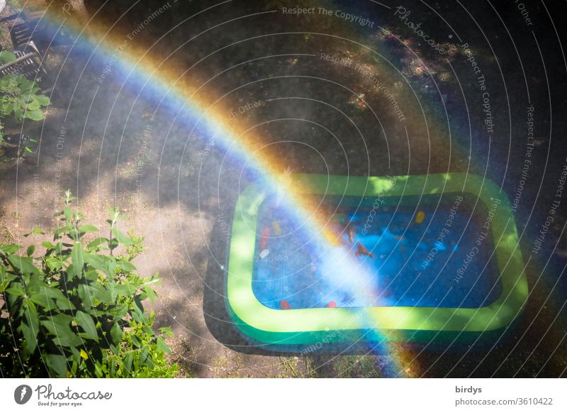 Paddling pool in a garden with rainbow and water drops. Bird's eye view Toys Infancy Rainbow cooling Prismatic colors Drops of water warm season Garden bush