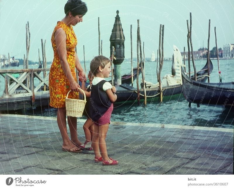 old l Pretty, young, fashionable mother with two daughters on summer vacation, are standing in the port of Venice. Mother with children watches curiously ships and boats in the sea. Family outing in Italy in the 60s. Nostalgic, old 60's family photo