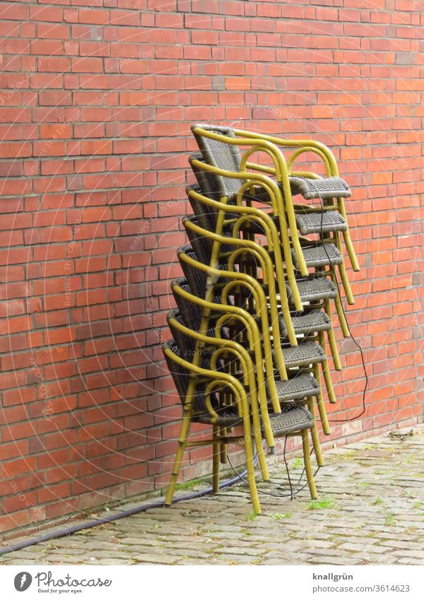 Eight secured basket chairs stacked one on top of the other in front of a red-brown brick wall Chair Stack Restaurant corona crisis Deserted Exterior shot