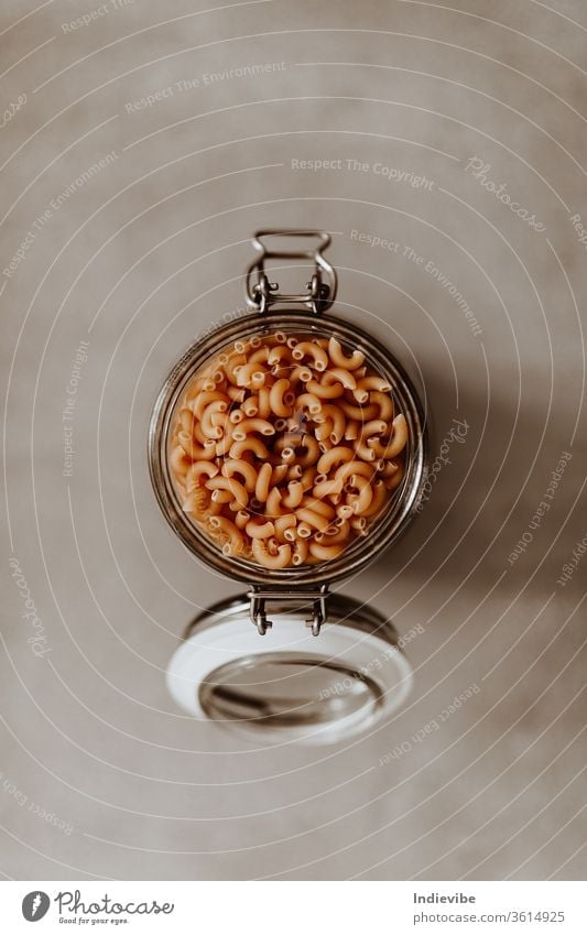 Top view closeup of a glass jar container full with uncooked pasta on grey background air tight basics bulk pantry cooking corona coronavirus dry durum
