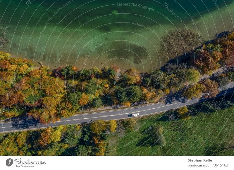Aerial view of road with a car in autumn forest next to a touquise colored lake. top countryside drone highway travel beautiful transportation landscape aerial