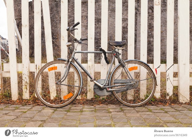 Gray, old, vintage and retro bicycle, padlocked on a wooden fence painted white in the city of Ghent, in Belgium, Europe. bike gray color ghent belgium europe