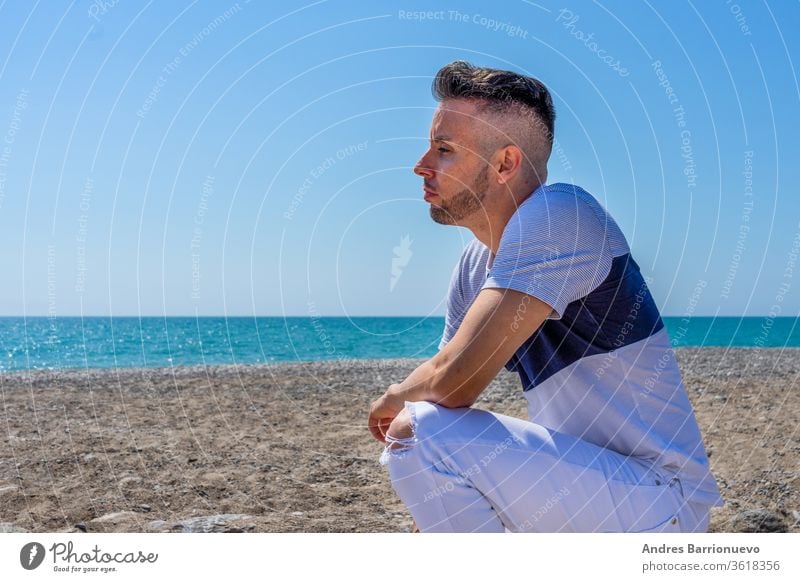 Young man in white pants and modern styling posing on the beach of the Mediterranean Sea in Burriana pleasure holiday toned fashion sky tourist pose wind tanned