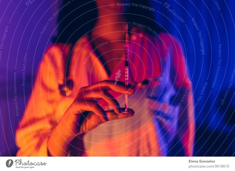 Doctor holding COVID-19, сoronavirus vaccine in the syringe using for prevent infection in ultraviolet neon light. Medicine and Healthcare concept. doctor