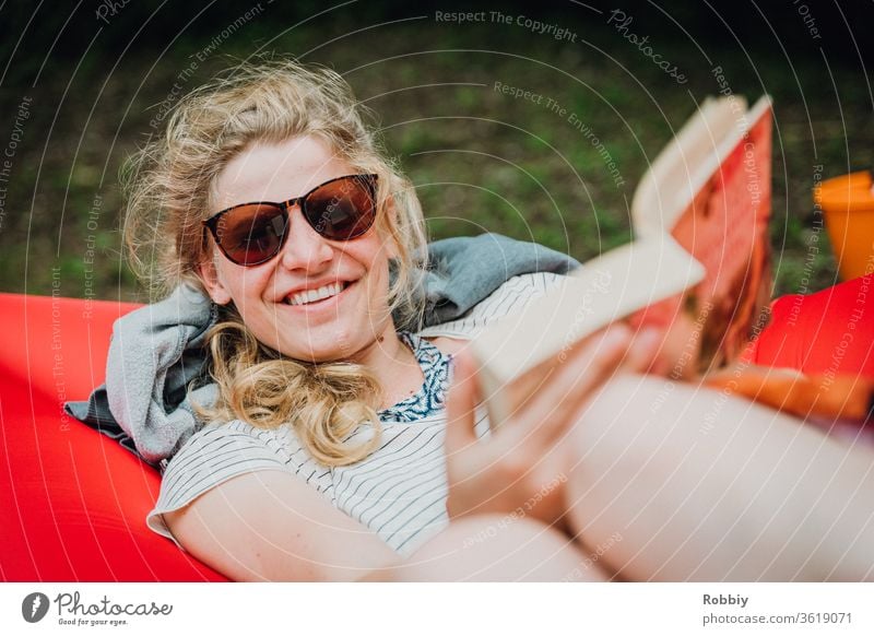 Young woman reading a book while lying on a lamzac on vacation and smiling friendly into the camera Book Reading Literature Lie Smiling Sunglasses relax chill