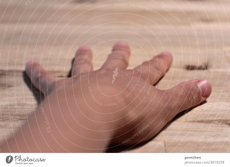 A left, female, tanned hand with spread fingers lies on a wooden tabletop.  Dominance by hand Skin color Fingers Tabletop fingernails Left Thumb Underarm