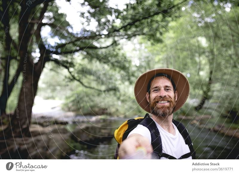 young man with beard hiking along a lake route with trees and shaded areas taking a selfie travel nature adventure outdoor lifestyle landscape mountain tourism