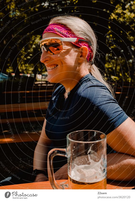 Bike tour break in the beer garden Bavaria Beer garden Shandy Drinking To enjoy relax Laughter cheerful fortunate relaxed Athletic Jersey sunglasses Young woman