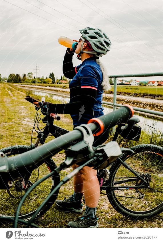Young woman drinking from a bicycle bottle while mountain biking Mountain bike Bicycle Sports Athletic Athlete fun Helmet Jersey Exterior shot Fitness Cycling