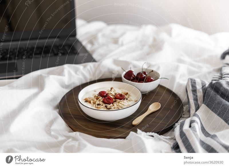 Yoghurt with muesli and cherries on a white duvet and a laptop Cereal Breakfast Bed Bedroom home office fruit Cherry bowls Dessert Oats White Organic Spoon