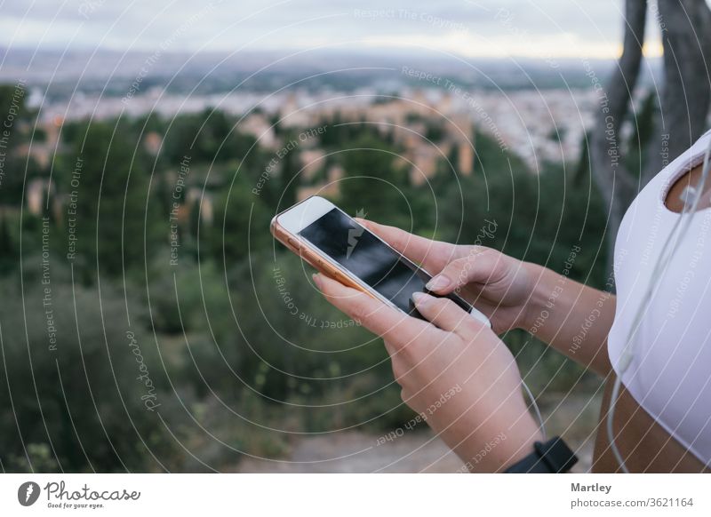 Hands of a young girl using the phone in nature after exercising. Crop an irecognizable woman using the mobile tracking app while exercising outdoors activity