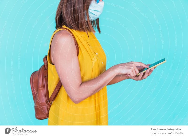 Portrait of a young woman in front of a turquoise background with a protective mask. With mobile phone. Summertime and coronavirus concept Technology Woman