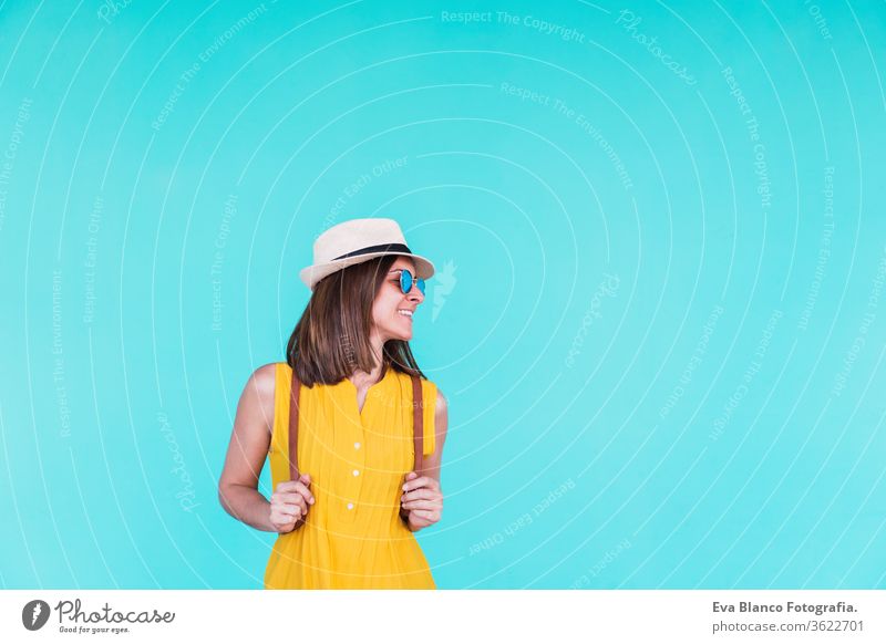 portrait of happy young woman outdoors over turquoise background. Summer time mobile phone summer sunglasses yellow hat backpack city urban lifestyle smiling