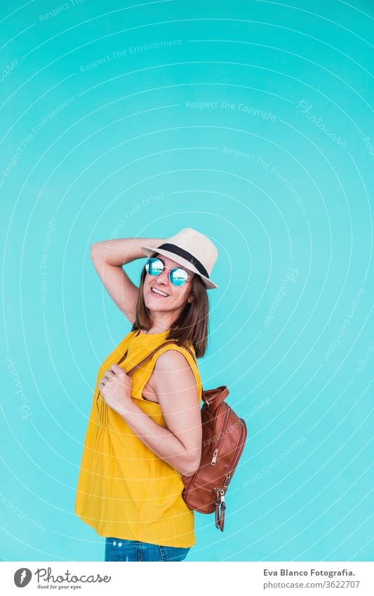 portrait of young woman outdoors over turquoise background. Summer time mobile phone summer sunglasses yellow hat backpack city urban lifestyle happy smiling