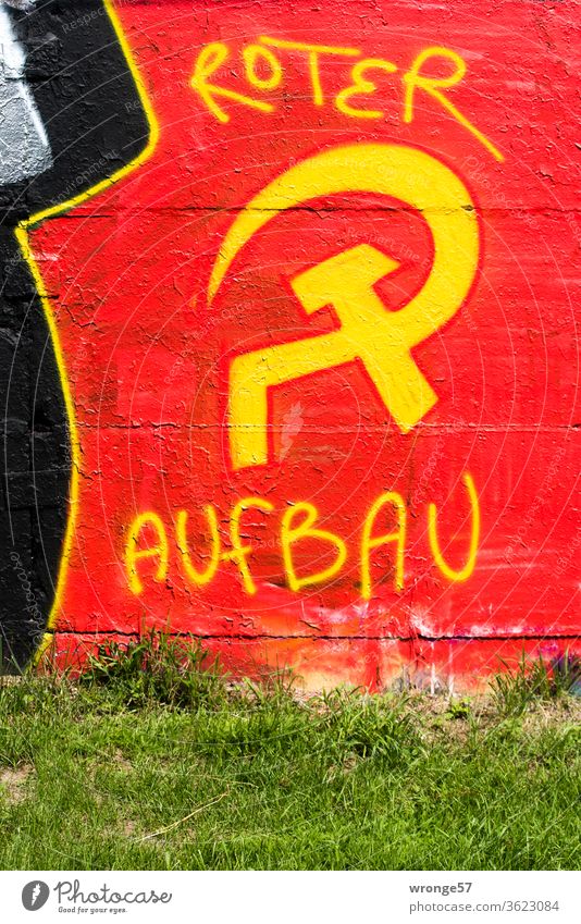 Graffiti Hammer and sickle with yellow paint sprayed on a red background on a wall and completed with the words red construction hammer and sickle yellow color