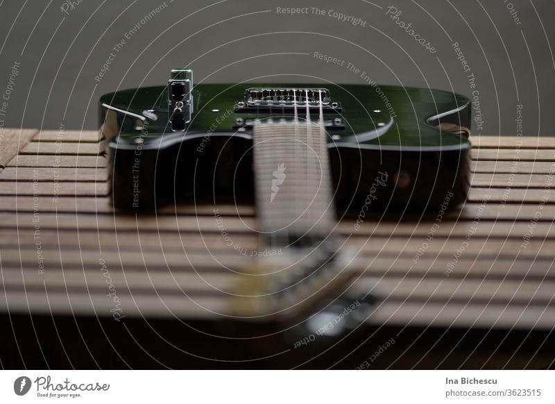 A black electric guitar on a wooden board table photographed from the guitar head perspective. The focus is on the side holder and knob. Egg guitar Guitar