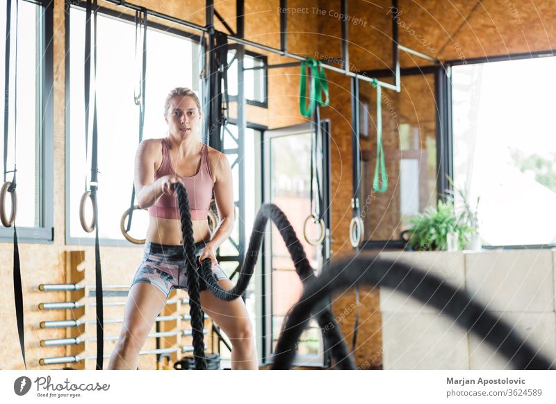 Young woman in the gym training crossfit on the ropes beautiful strength tough equipment sports sporty endurance fitness attractive alternating pulling energy