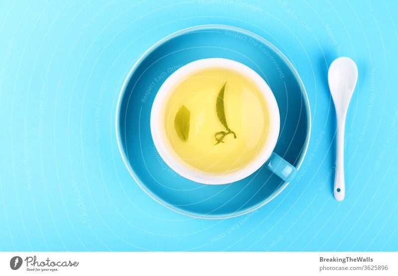 Blue cup of green oolong tea over blue background Tea yellow herbal spoon white saucer paper pastel closeup elevated top view high angle directly above hot