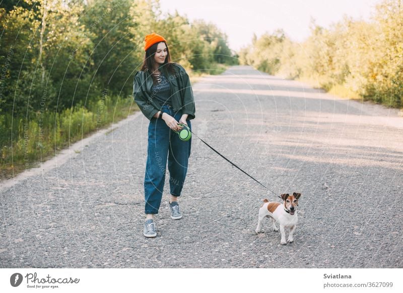 Cute modern teen girl in a green jacket and orange hat walks with her dog in nature. Pet, care, friendship. park young walking woman animal pet summer outdoor