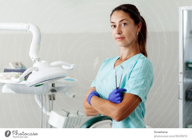 A female dentist is sitting in a chair and smiling while holding tools in her hands. dentistry office care clinic doctor equipment health hygiene medical