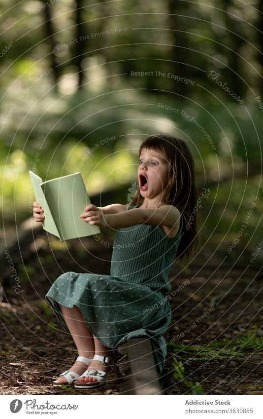 Shocked girl reading book in park shock amazed astonish surprise wow preteen story interesting garden summer dress kid excited child adorable cute childhood