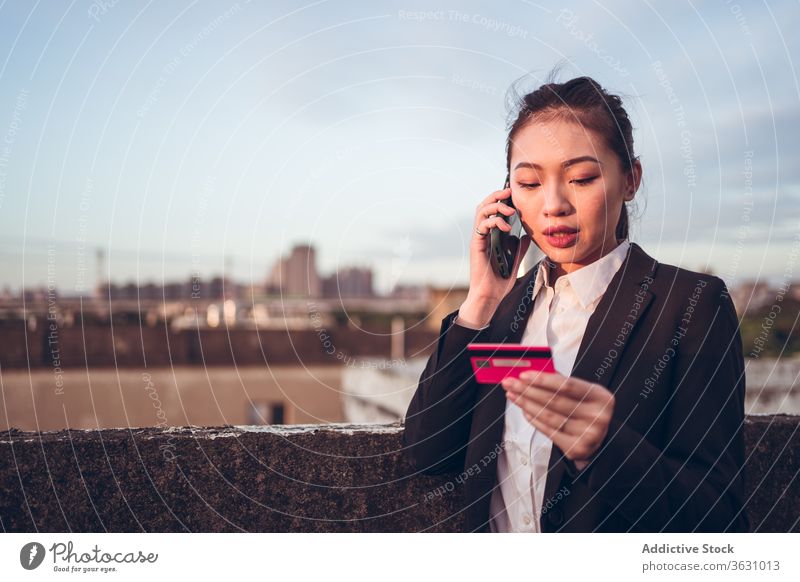 Busy ethnic woman with credit card speaking on phone phone call busy serious talk smartphone problem discuss formal young asian businesswoman conversation