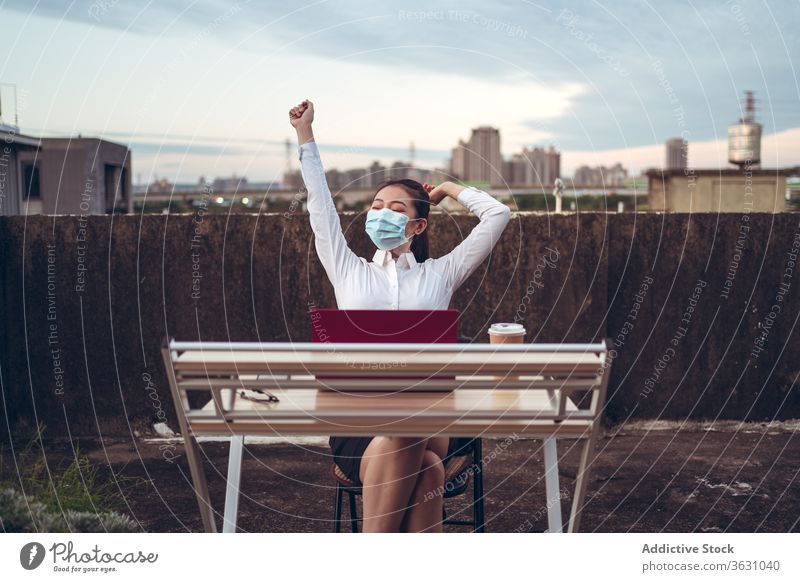 Cheerful woman having break during remote work with laptop relax busy rest rooftop mask workplace young asian female employee ethnic formal device gadget