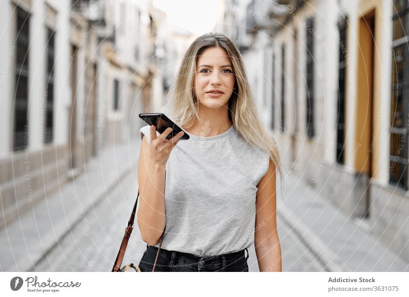 Positive young woman with smartphone walking on street city using happy style message browsing female mobile lifestyle device gadget stroll urban smile trendy