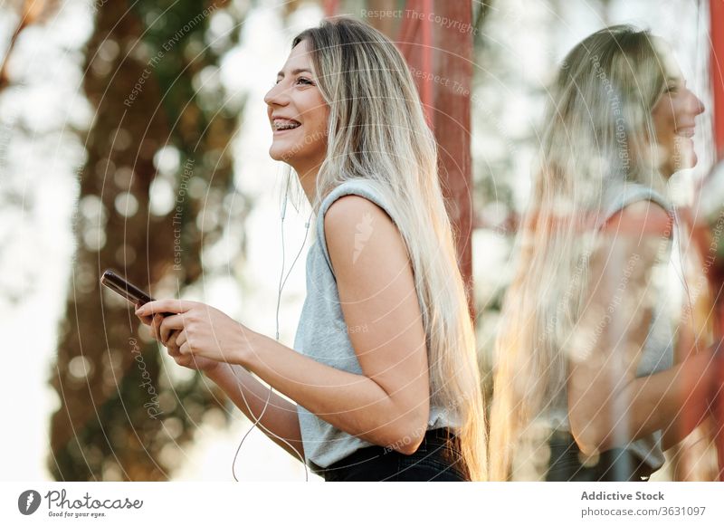 Cheerful woman with earphones using smartphone on street happy cheerful listen browsing young female music enjoy device gadget lifestyle smile online song