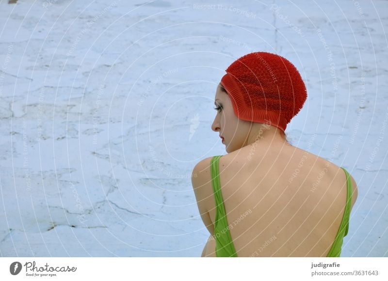 The girl with the beautiful red bathing cap and green swimsuit is sitting in the empty non-swimmer's pool. A summer love. Girl Woman Swimwear Bathing cap