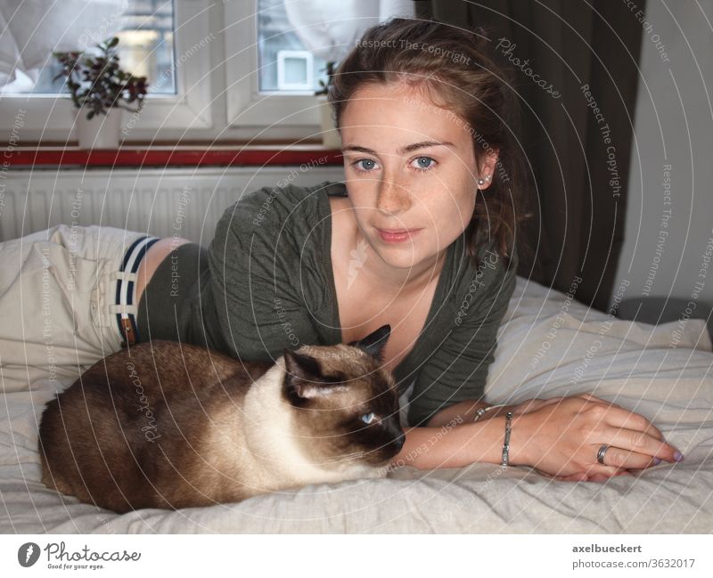 young woman lies at home with cat on bed Young woman Cat Siamese cat Pet Bed Lie youthful pretty smile relax room fond of animals Bedroom Animal Relaxation Day