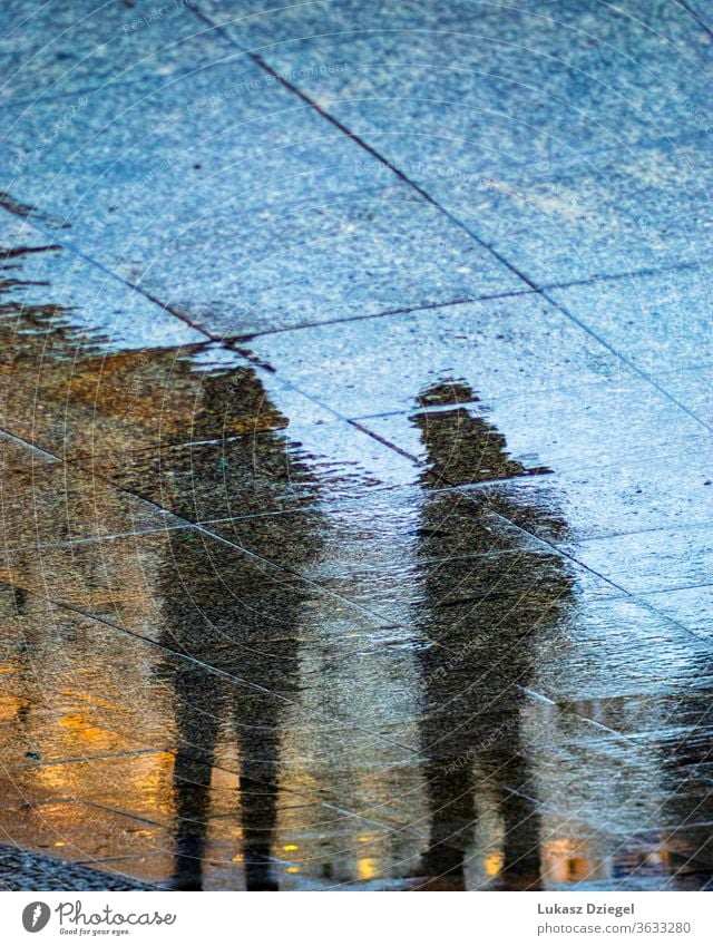 Silhouettes of people reflecting in the sidewalks wet from rain art shape creative blurry depressed surface ground mood life mirrored silhouette reflection