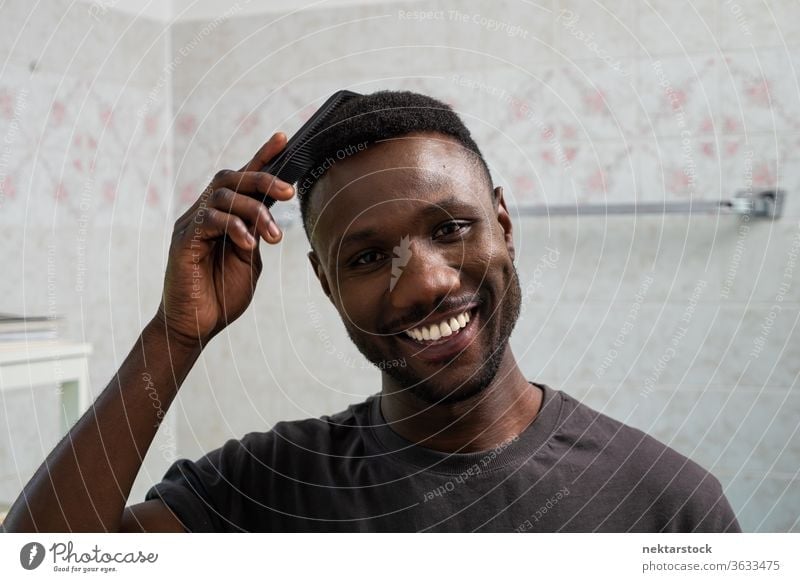 Handsome Black Man Smiling and Combing Hair in Bathroom combing hair face hairstyle man 1 person African ethnicity smile toothy smile smiling lifestyle