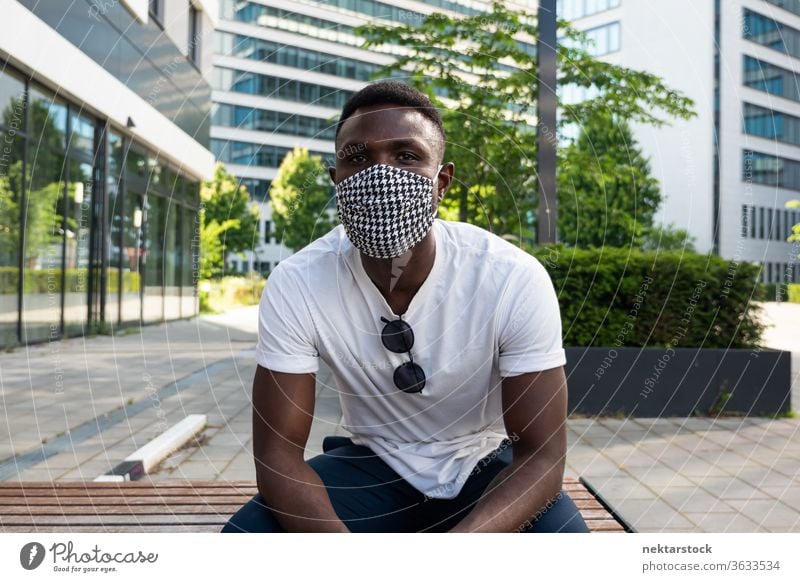 Young Black Man Wearing Face Mask Looking at Camera 1 person African ethnicity man lifestyle looking at camera bench summer medium shot portrait relaxation