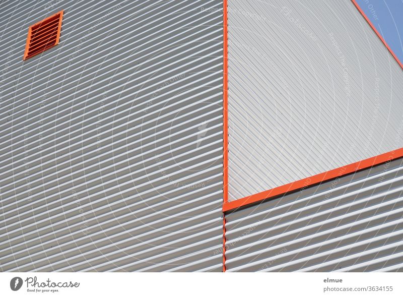 Partial view from a frog's perspective of a functional building made of grey corrugated iron, orange edges and an orange square ventilation window built